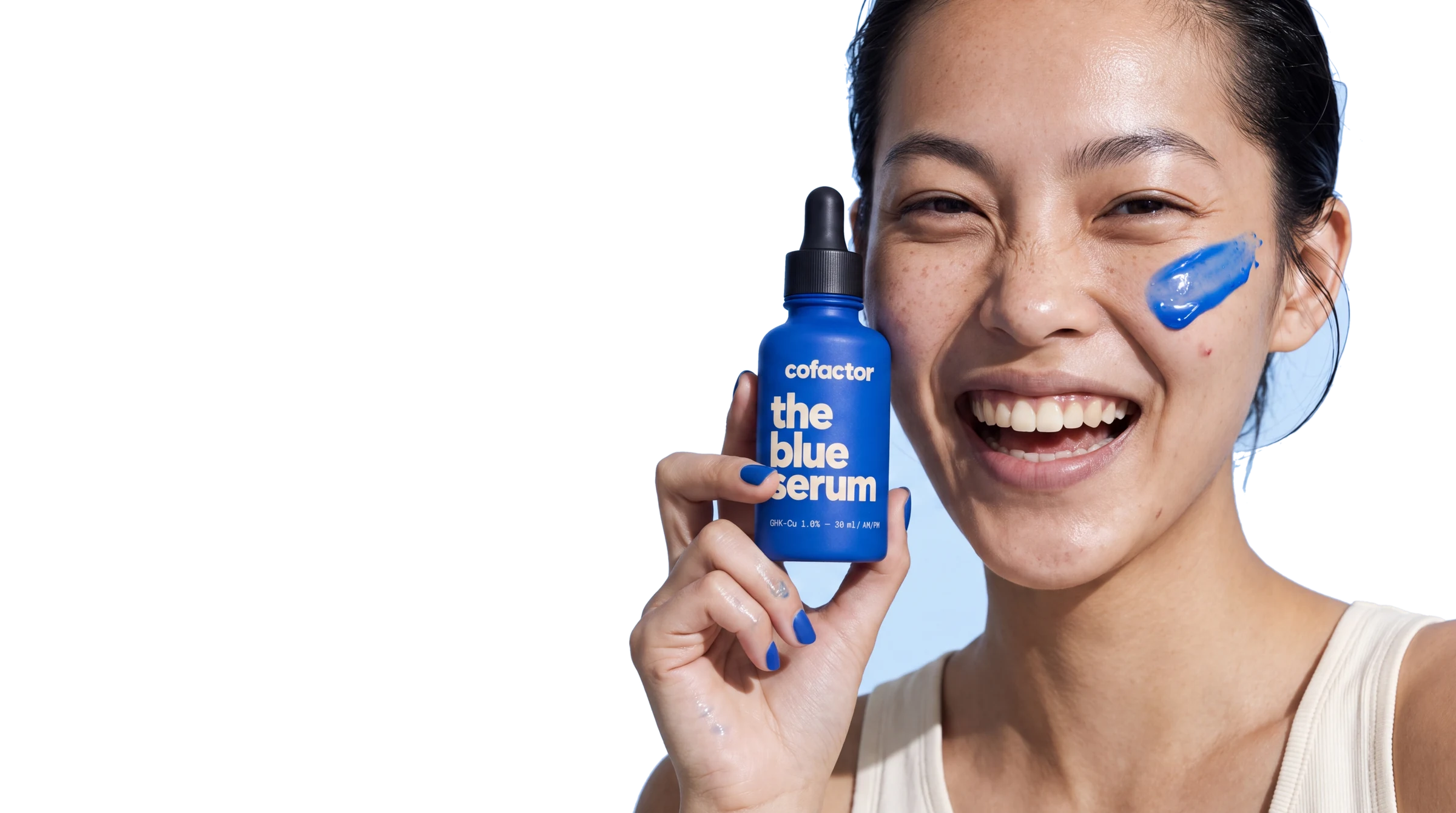 a woman laughing, holding the blue serum beside her jaw, a glossy cupric smear across her cheekbone, hard sun, one shadow